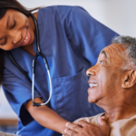 A Patient on a wheel chair with a nurse aid wearing blue clothes